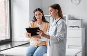 medicine, healthcare and people concept - female doctor with tablet pc computer talking to woman patient at hospital