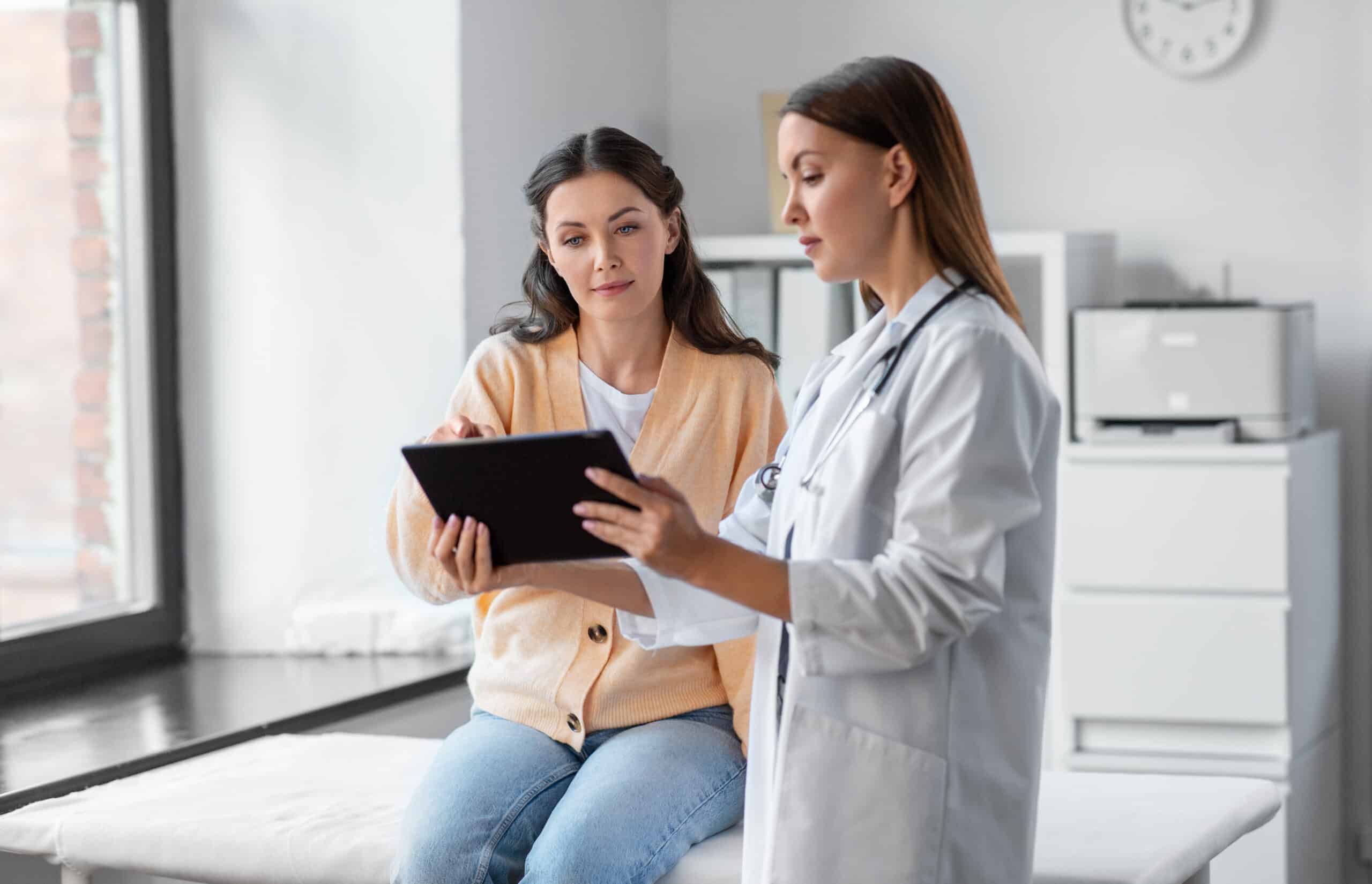 medicine, healthcare and people concept - female doctor with tablet pc computer talking to woman patient at hospital