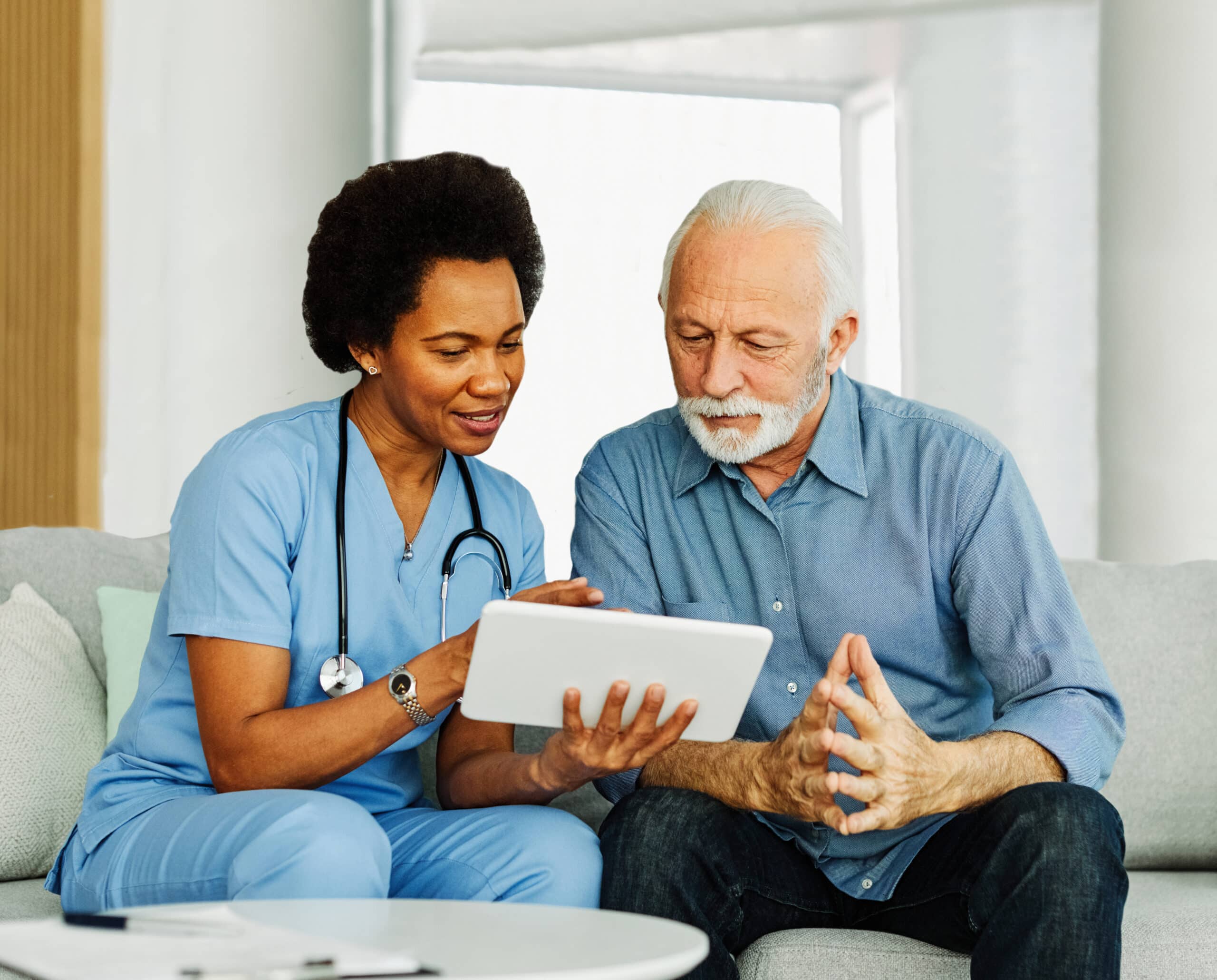 Doctor or nurse caregiver showing a tablet screen to senior man and laughing at home or nursing home